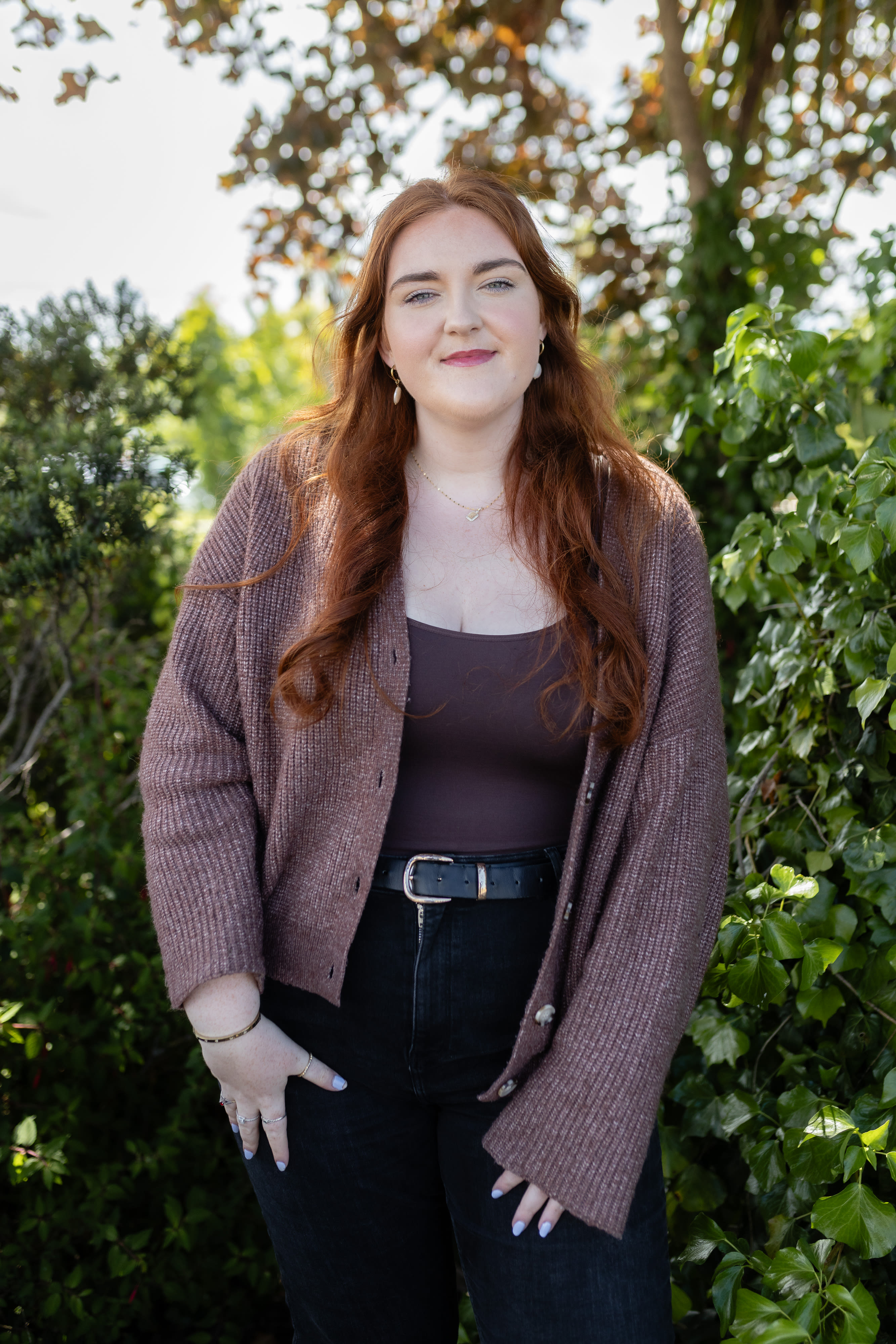 A redhaired woman standing in greenery.