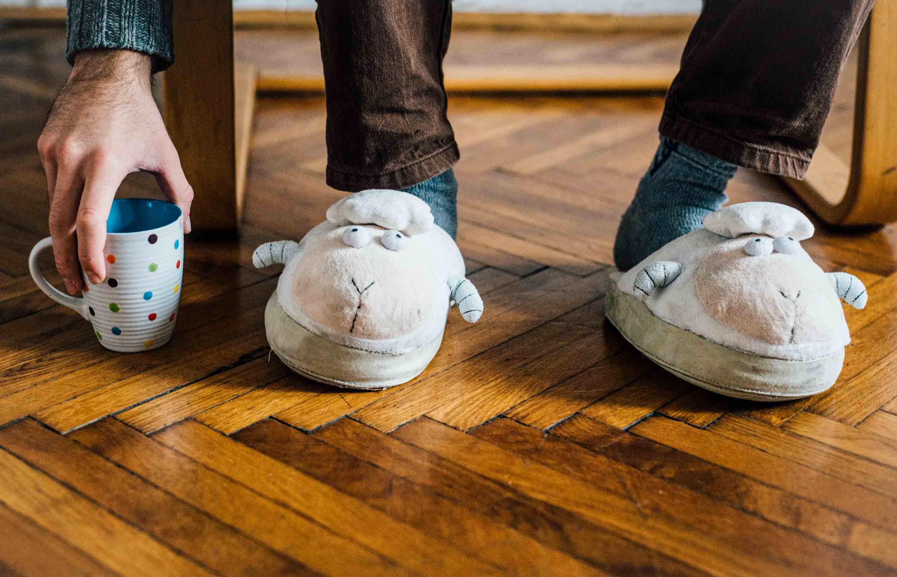 We’ve Got Families, Too: Life Insurance Stories From the Fabric Team - A man wearing comical fuzzy lamb slippers reaching down for his polka dot coffee mug placed on the wooden floor by his feet and in front of his chair leg.