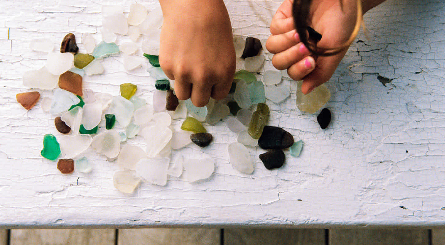 A child wearing pink nail polish plays with multicolored gemstones scattered on a table.