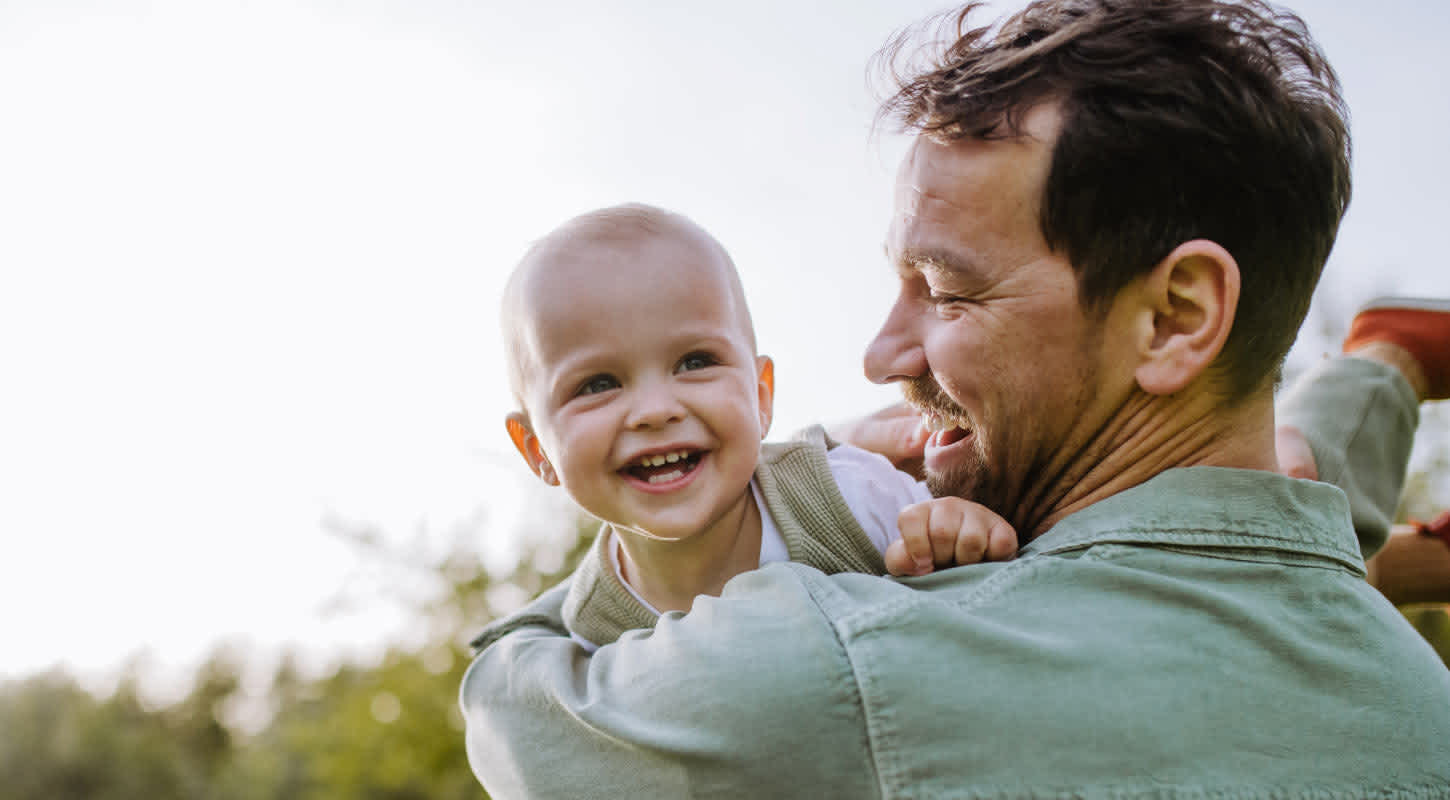A young man smiles while holding a smiling child over his shoulder.