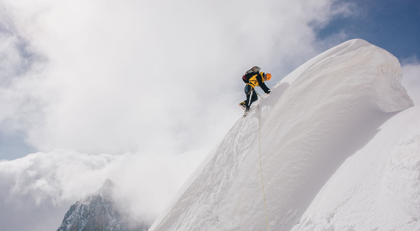 A climber reaches the peak of a snow-capped mountain. 