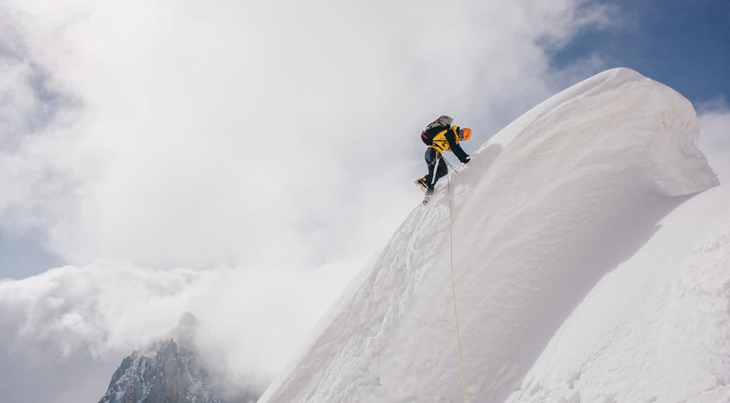 A climber reaches the peak of a snow-capped mountain.