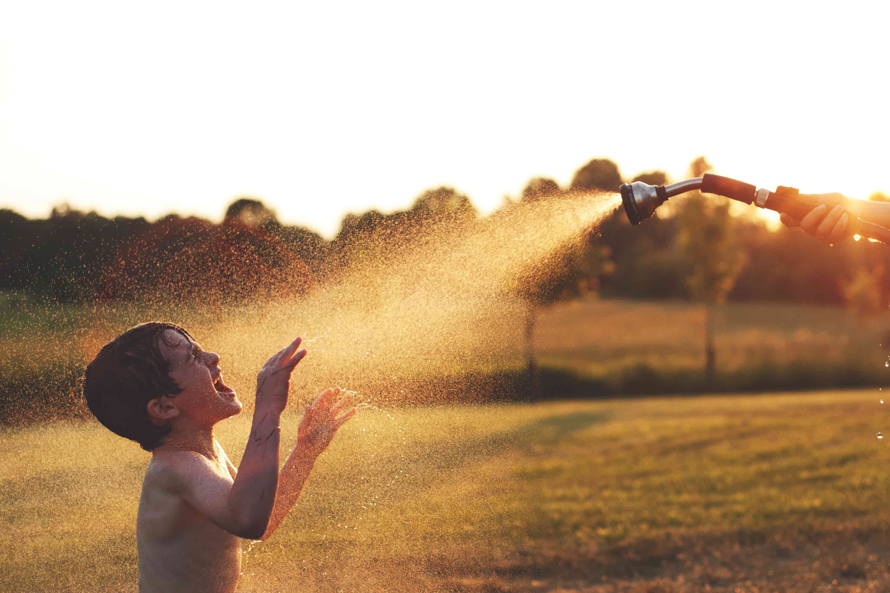 Summer financial to do list - boy playing in sprinkler outside