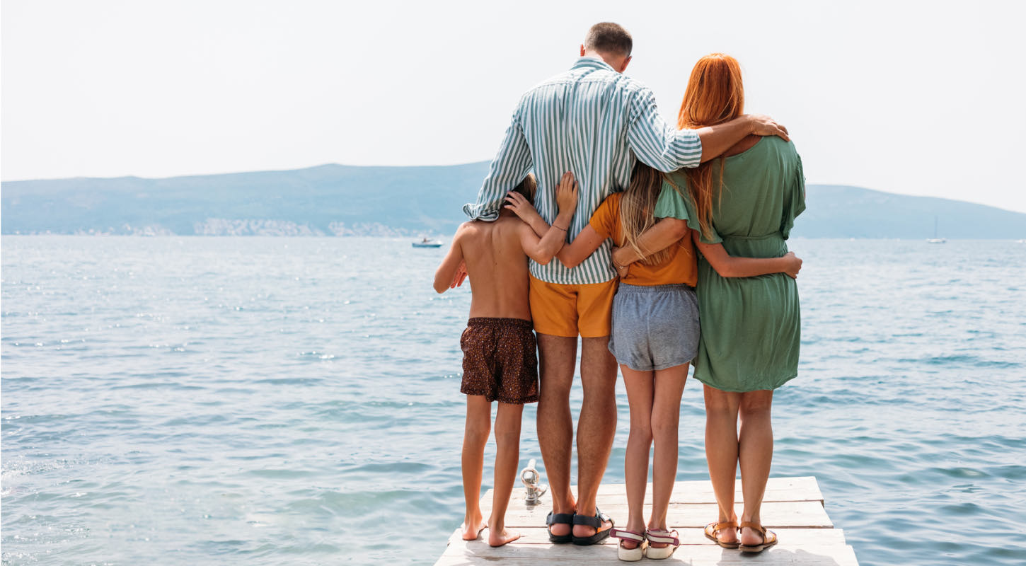 A family huddles together at the edge of a dock while looking out towards an expansive waterscape. 