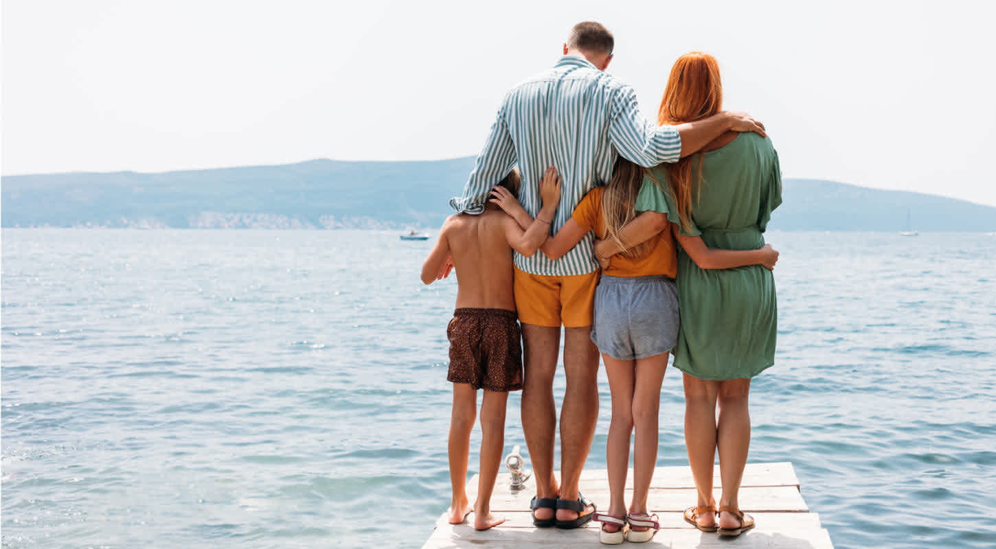 A family huddles together at the edge of a dock while looking out towards an expansive waterscape.