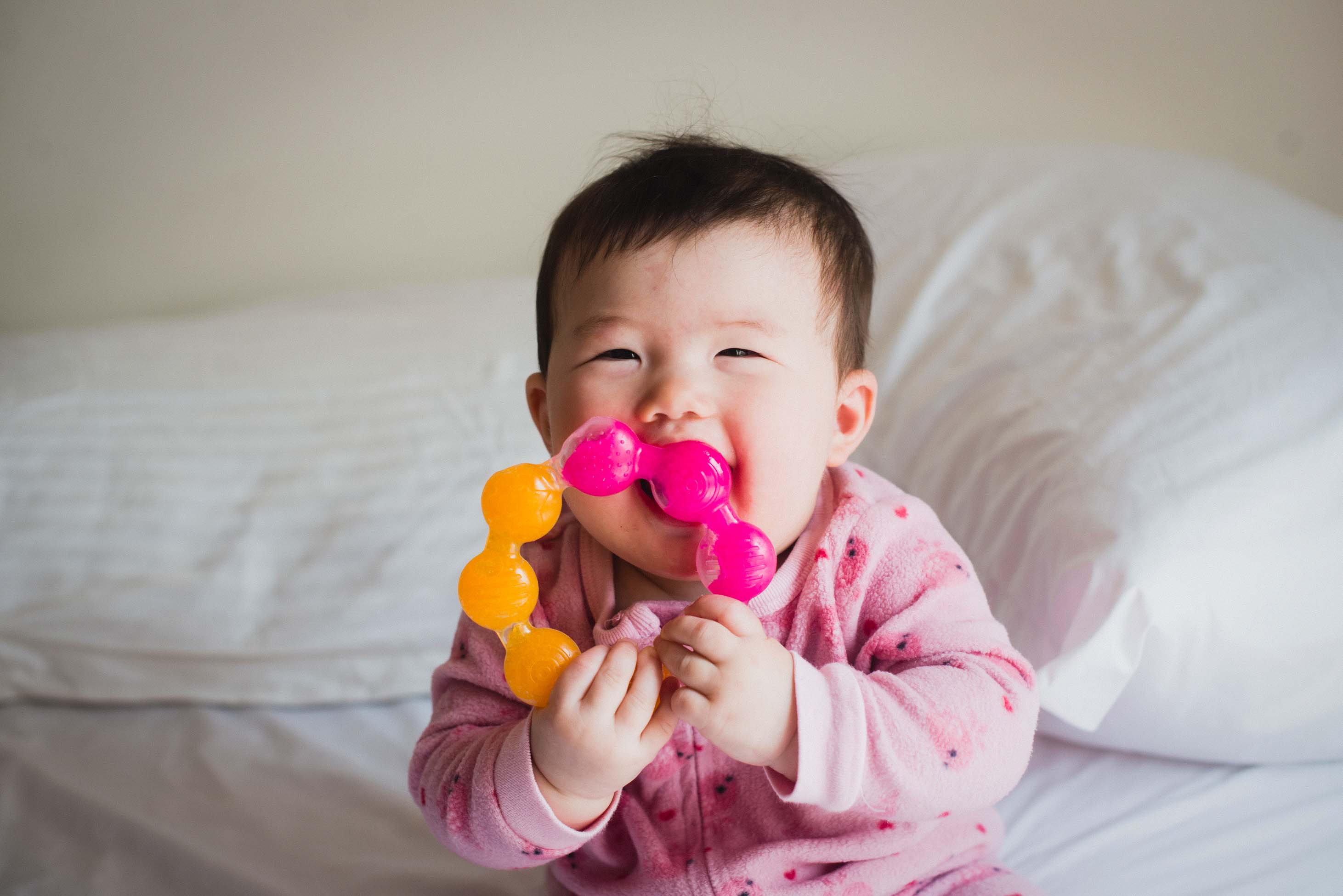 what to know during the first year of your child's life - smiley baby playing with teething toy