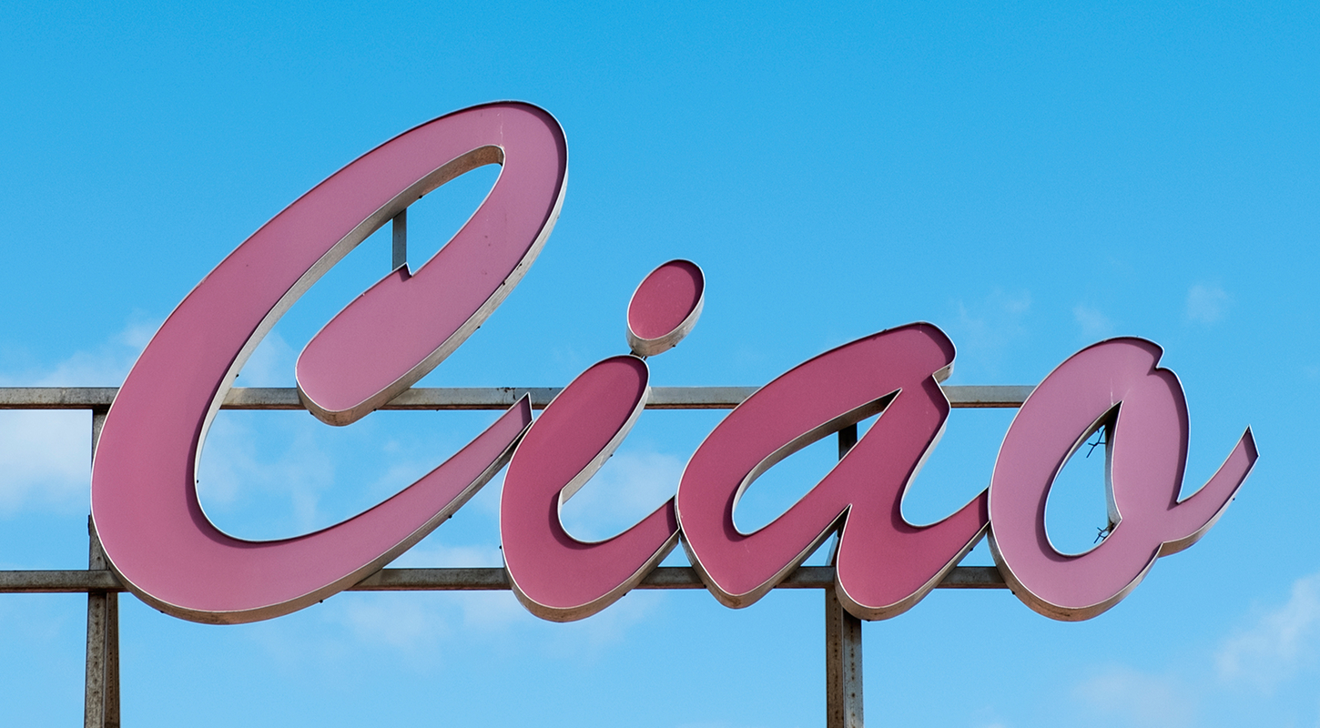 A pink billboard sign reads "Ciao" against a clear blue sky. 
