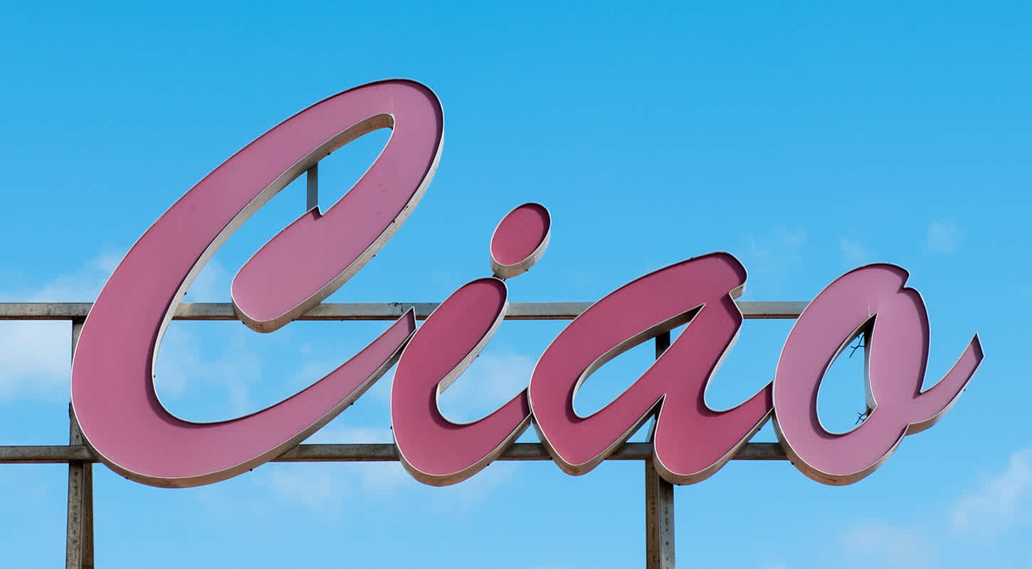 A pink billboard sign reads "Ciao" against a clear blue sky.