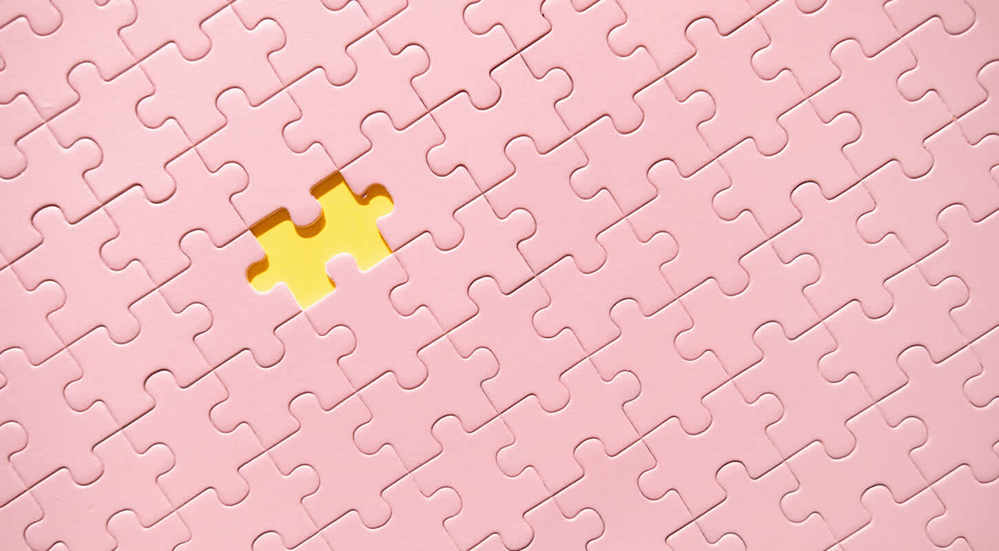 A yellow puzzle piece lies on top of a wide pink puzzle board, positioned as if ready to be placed.