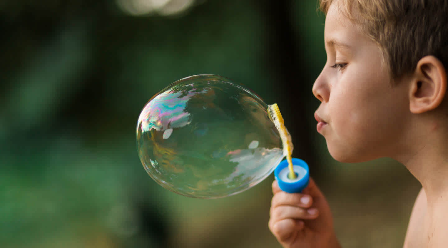 A young boy keeps his eyes closed while blowing a bubble with a bubble wand.