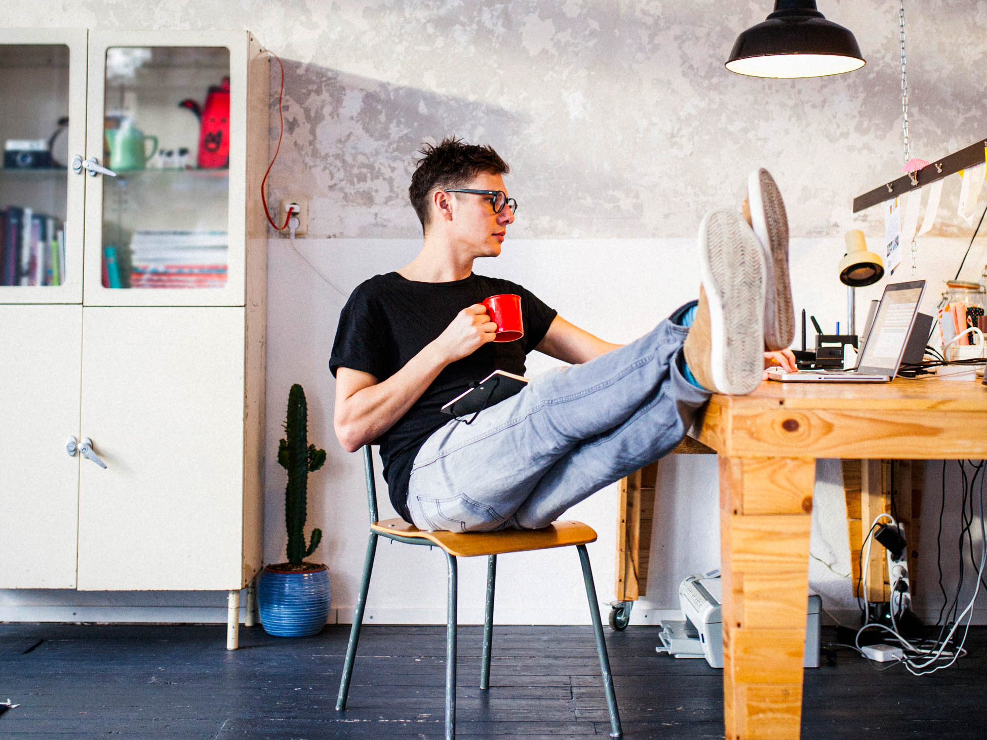 How to get life insurance - person in a t-shirt and jeans sitting with their feet up on a work table while drinking coffee