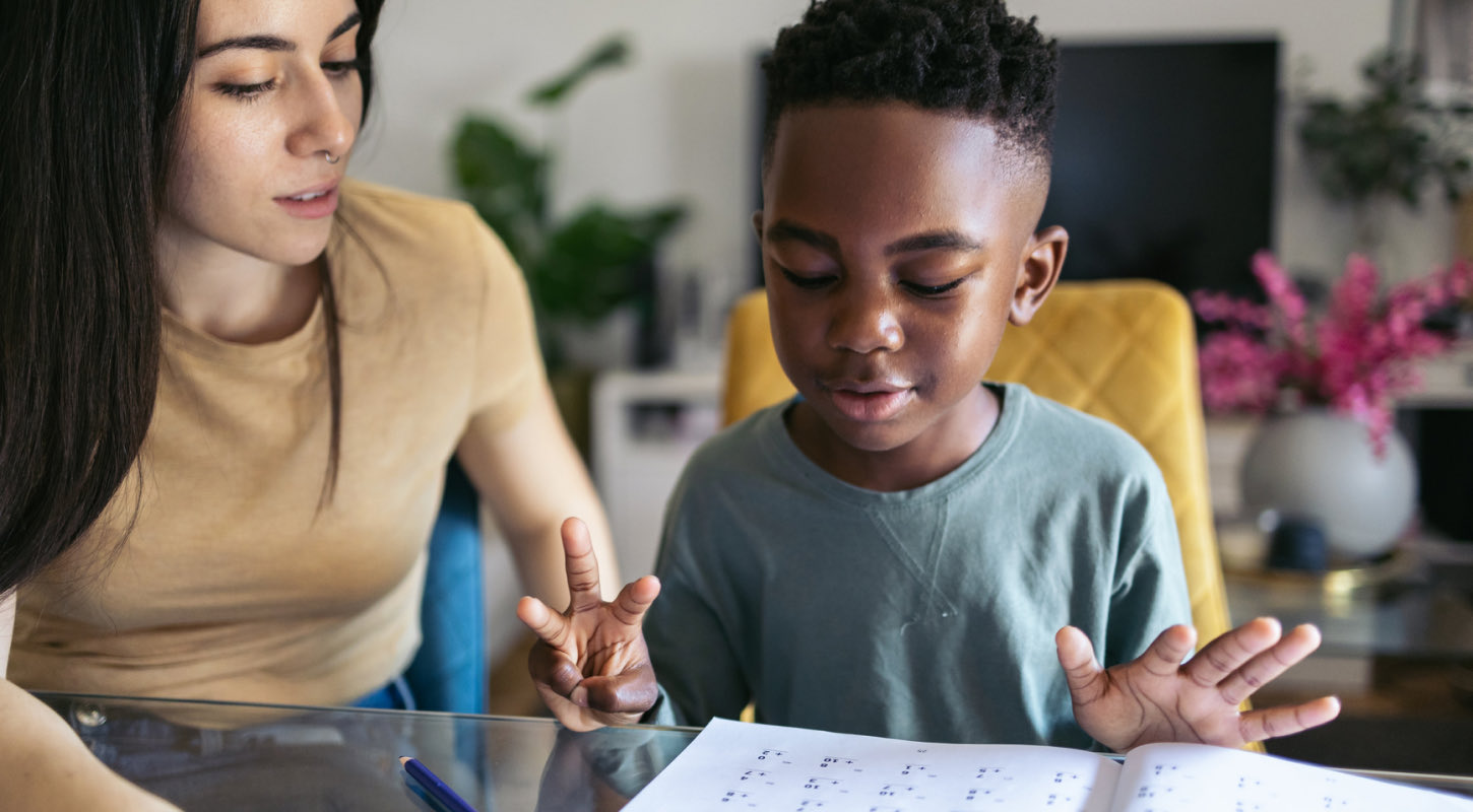 A young woman tutors a school-age boy at his home. 