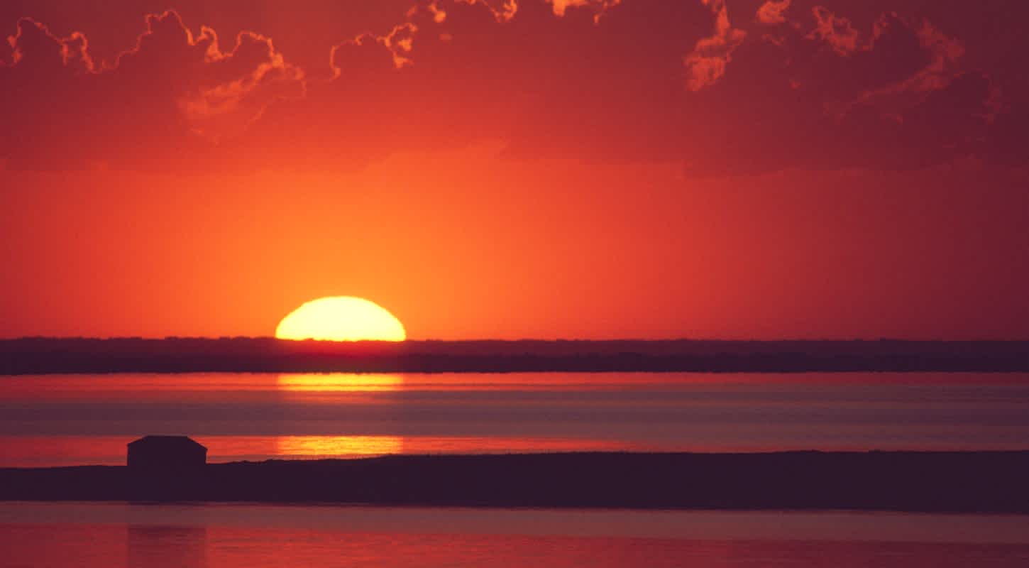 The sun sets over a calm body of water.