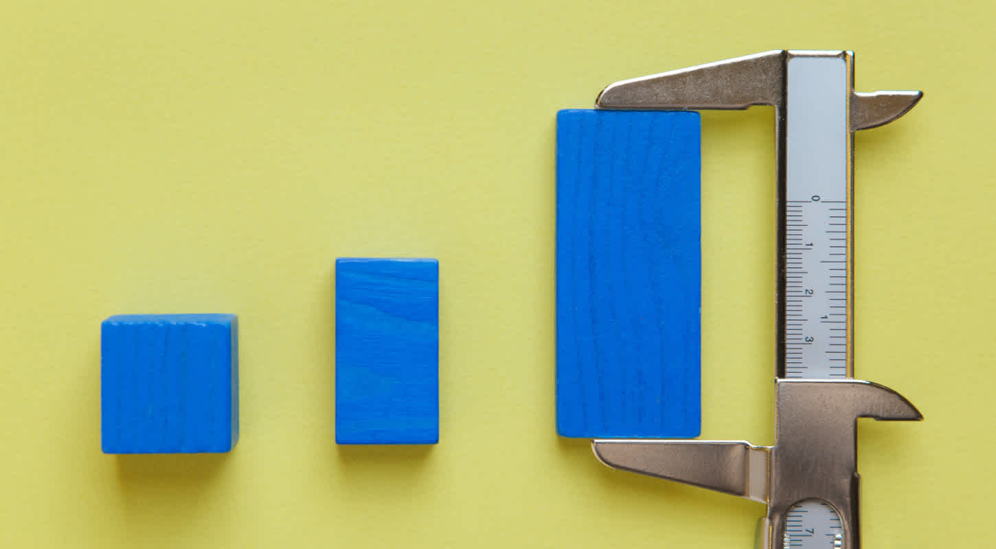 A caliper measures the dimensions of the largest of three blue blocks in a row of blocks.