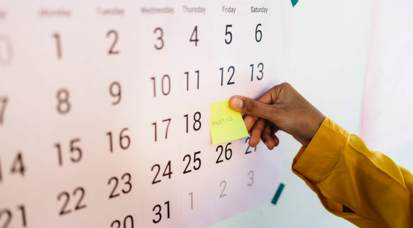 A person places a sticky note on a large calendar to mark their life insurance review date.