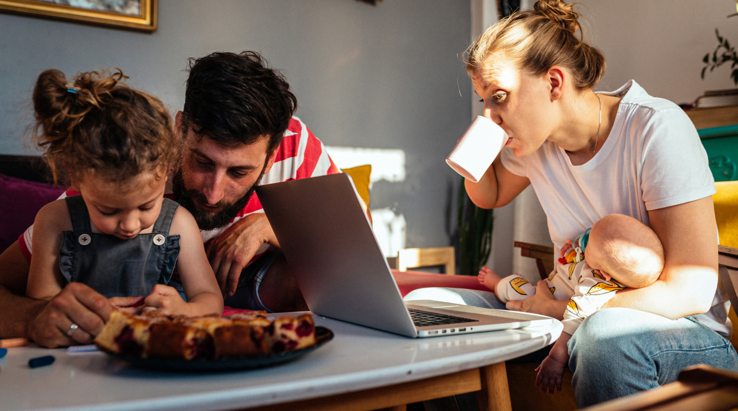A young couple working from home with their two infants enjoy a tart and coffee on the living room coffee table. 