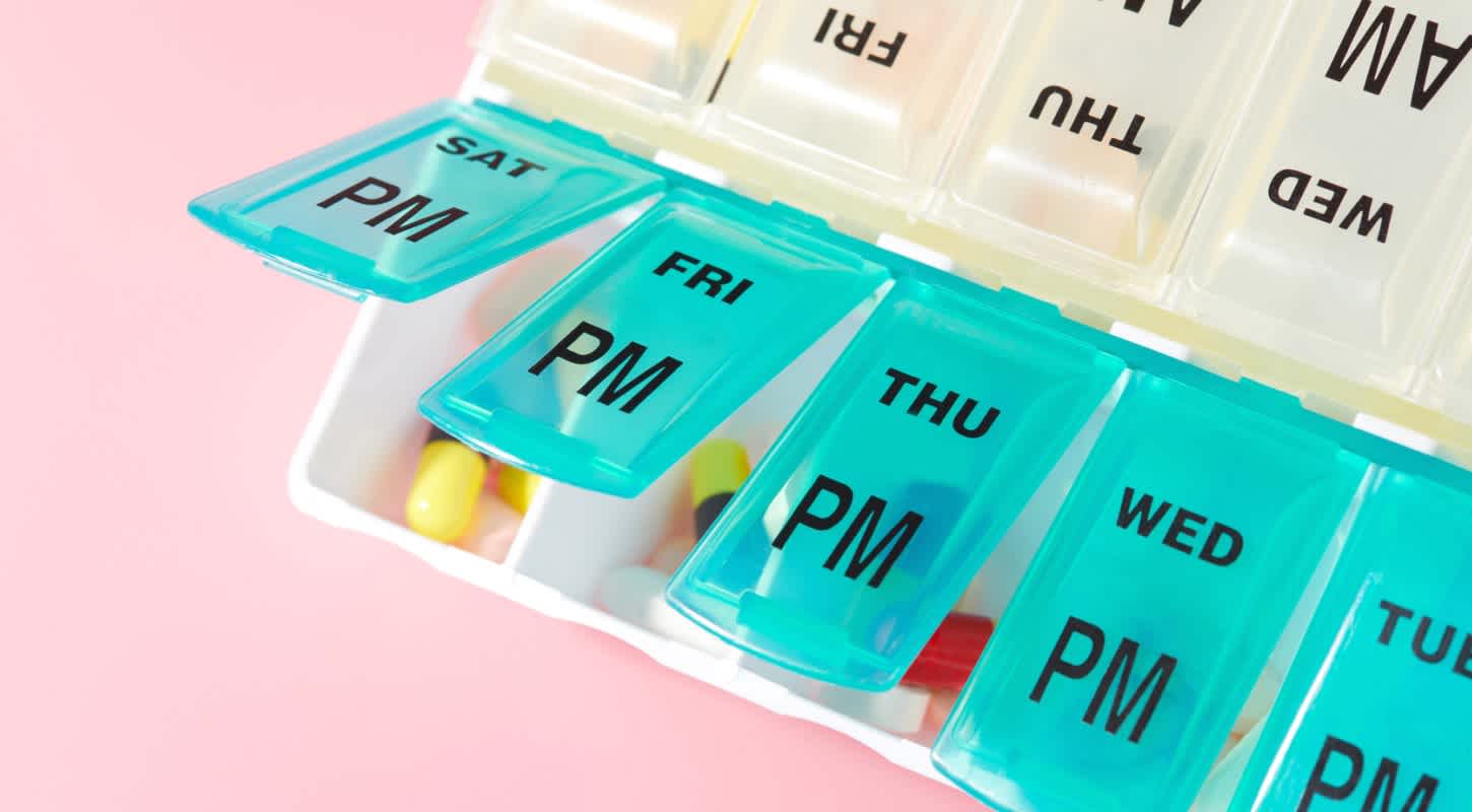 A weekly pill case with several open compartments organizes medication by day of the week and time of day.