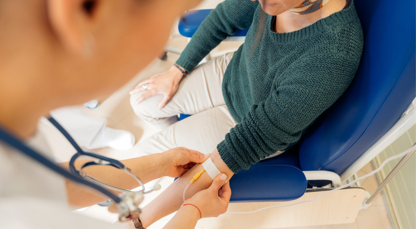 A young patient has an intravenous line (IV) inserted in their left arm by a medical professional. 