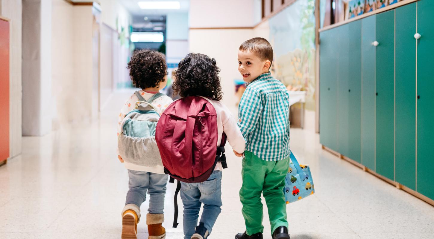 Three smiling elementary school children stroll down the hallway, backpacks on, ready for the day’s adventures.