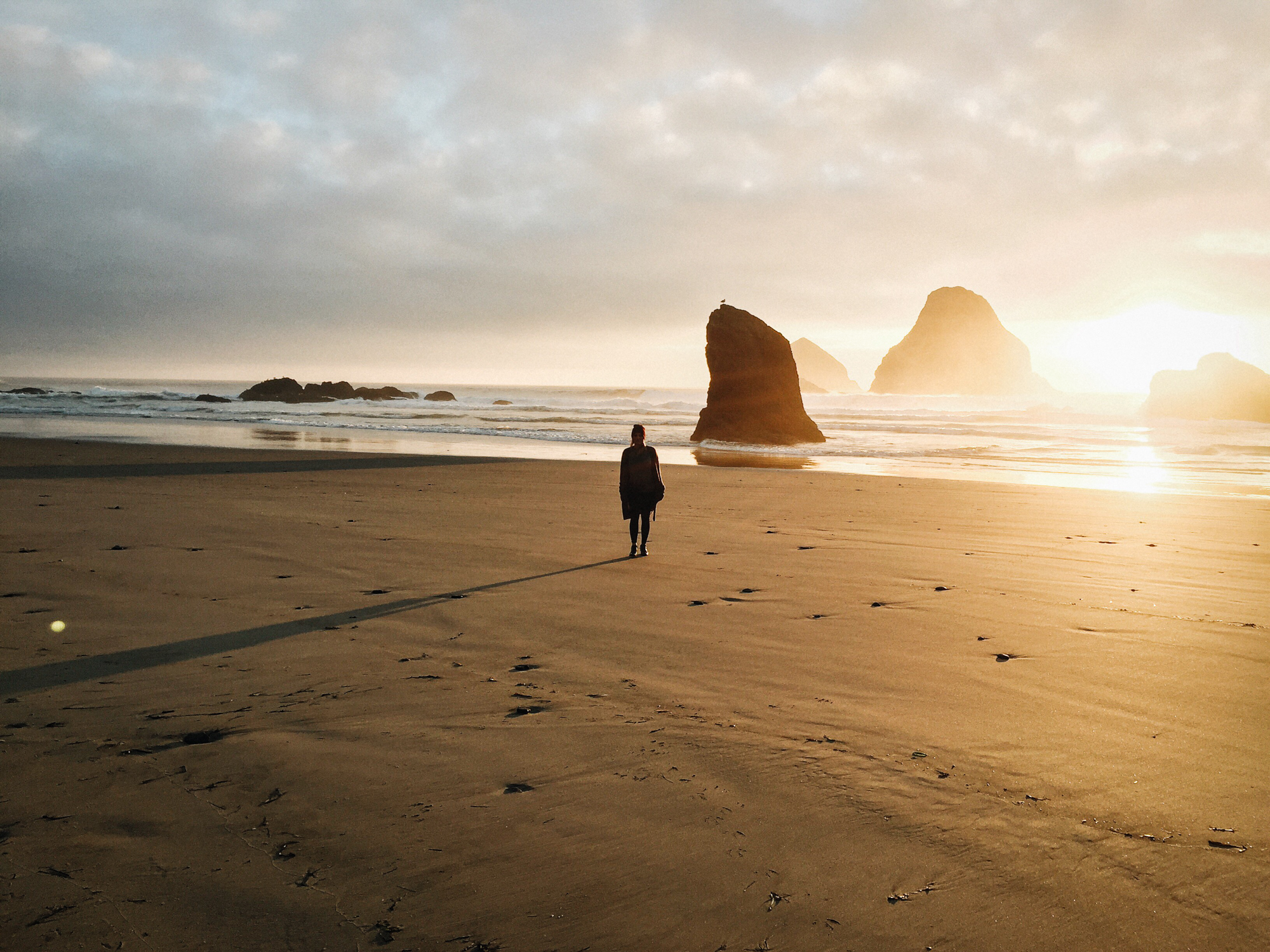 A beachgoer walks along the edge of the shore at sunrise. 