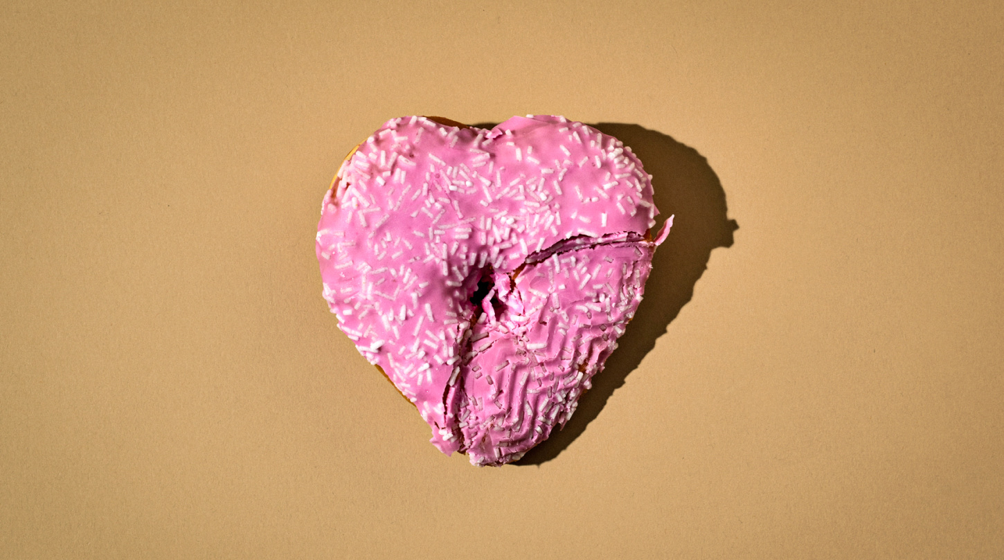 A pink heart-shaped donut with white sprinkles has been cut down the middle and imprinted by a tire.