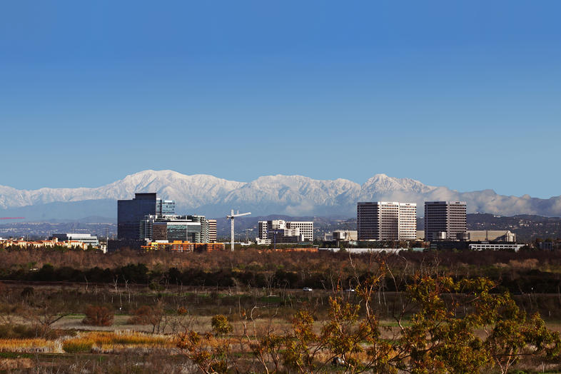 The Healthiest Cities in the United States for Families - Skyline of Irvine, CA with snowcapped mountains in the background against a blue sky. 