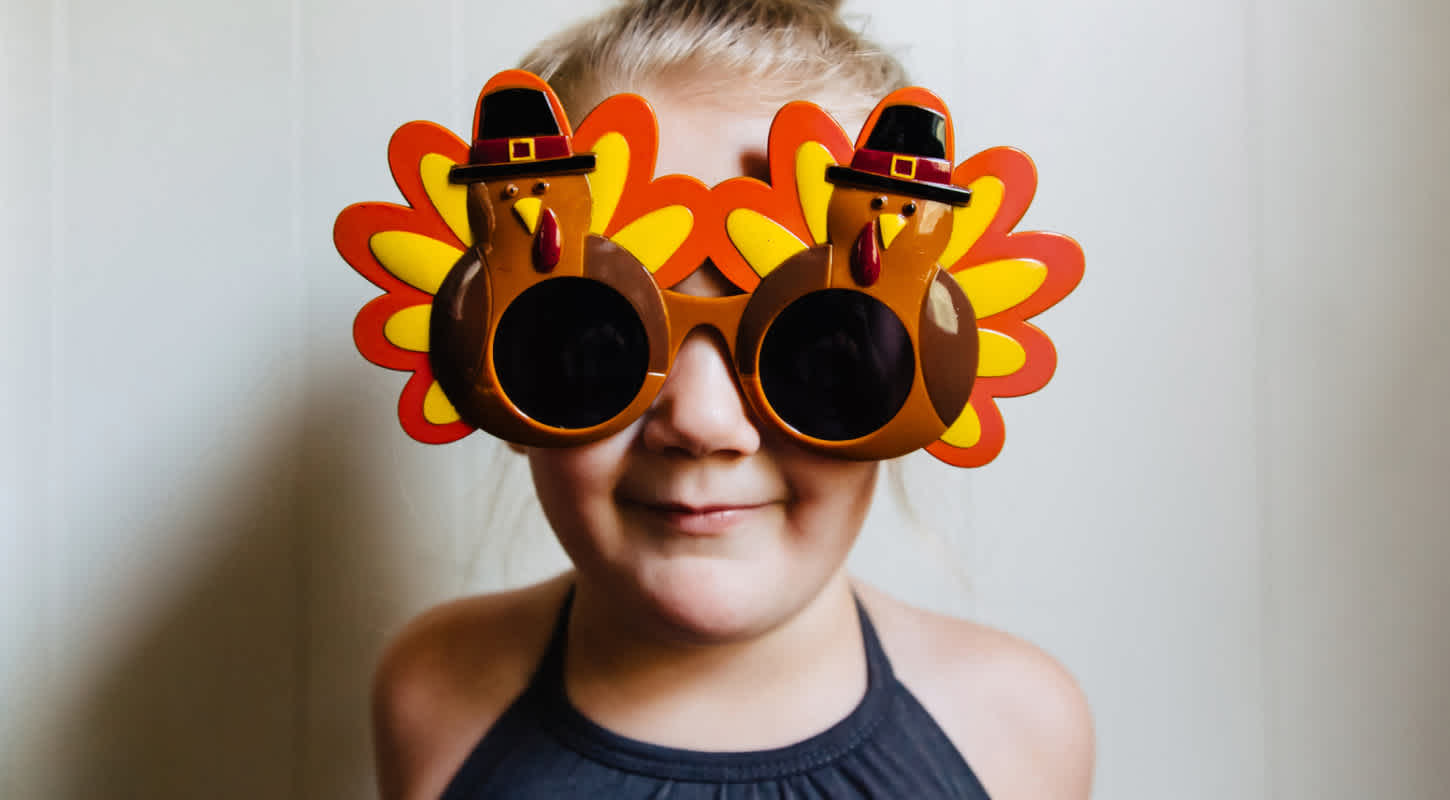 A young girl celebrating Thanksgiving wears turkey sunglasses.