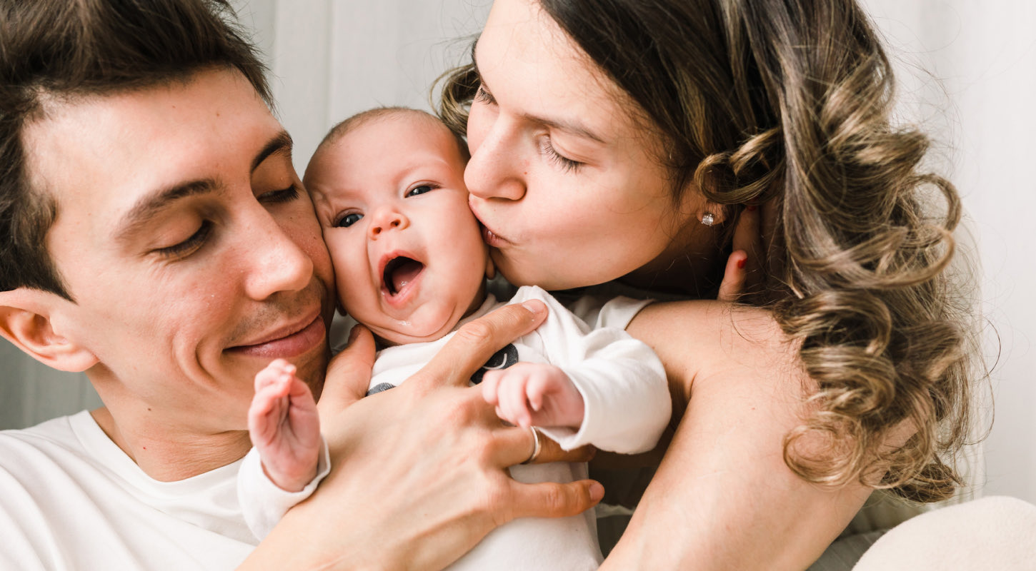 A newborn is cuddled and kissed by his young mother and father.