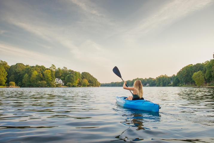 The Healthiest Cities in the United States for Families - A blonde woman kayaking on a body of water in Cary, NC on an overcast day. 