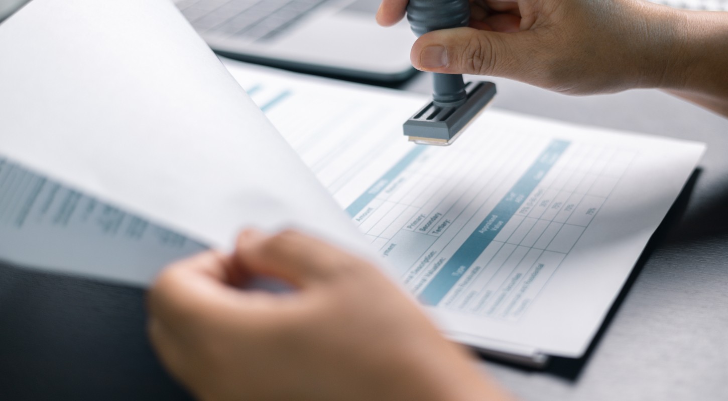 A close-up of a hand holding a rubber stamp poised over an insurance document, symbolizing the approval process for a life insurance claim.