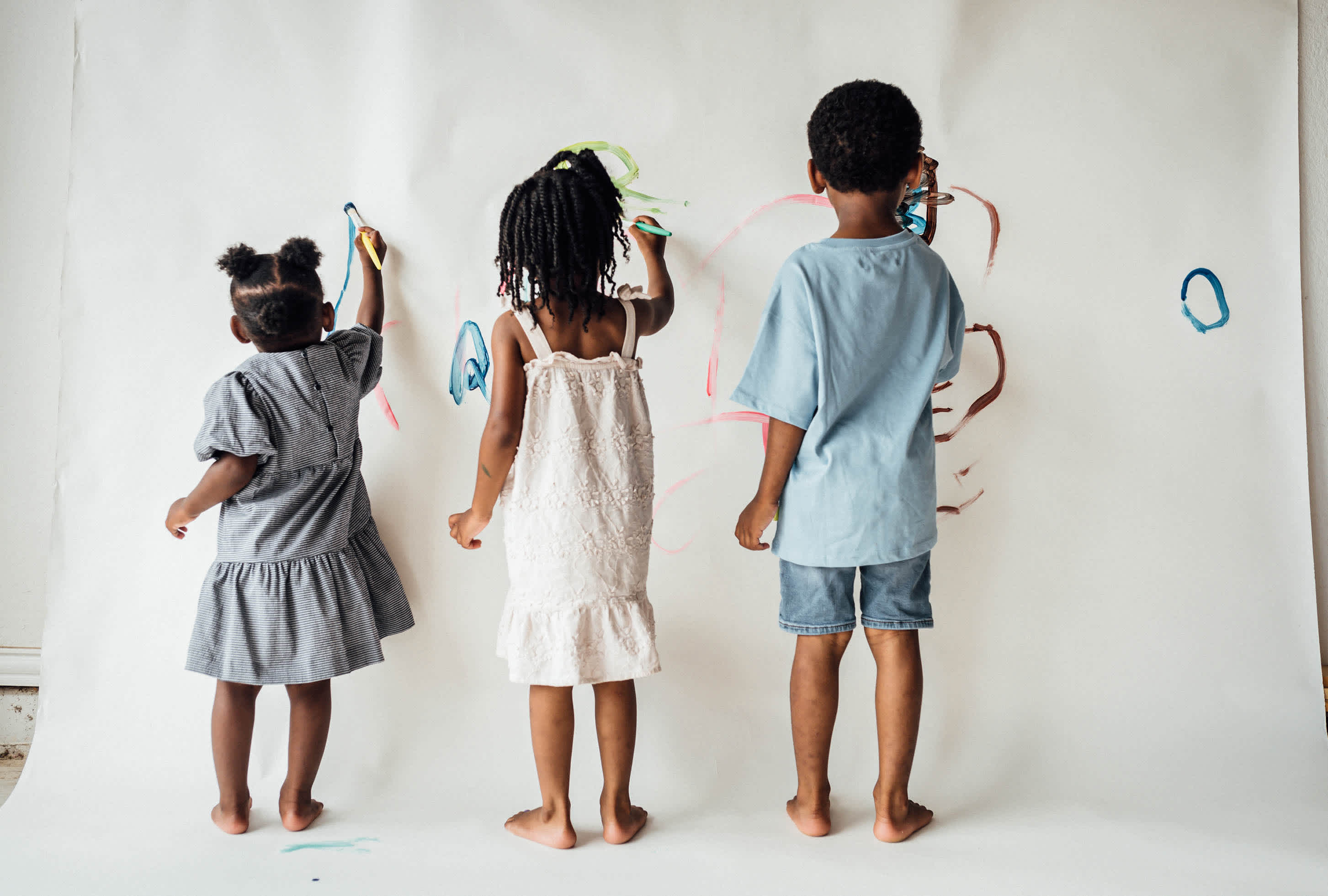 three kids of varying heights scribbling with markers on a giant paper on the wall - life insurance laddering