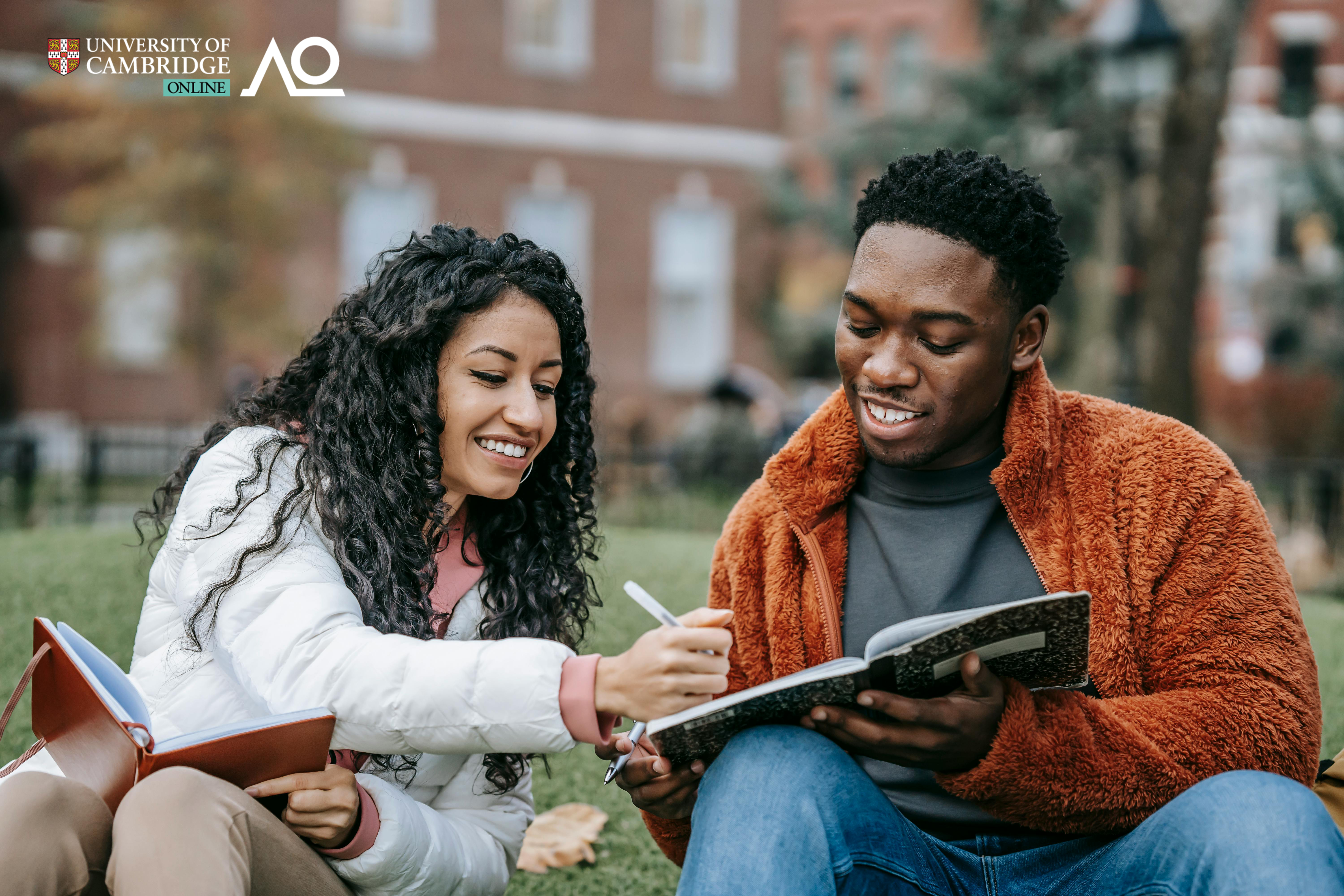 A young woman and man sitting on the grass and studying together.