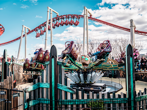 Åkattraktion med snurrande säten i förgrunden och en slingrande berg-och-dalbana i bakgrunden under en delvis molnig himmel.