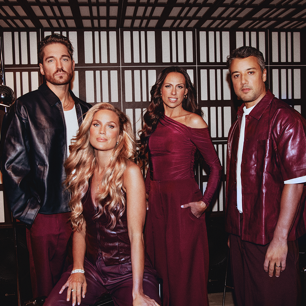 Fyra personer poserar inomhus mot en geometriskt mönstrad vägg, iklädda koordinerade vinröda och läderkläder.