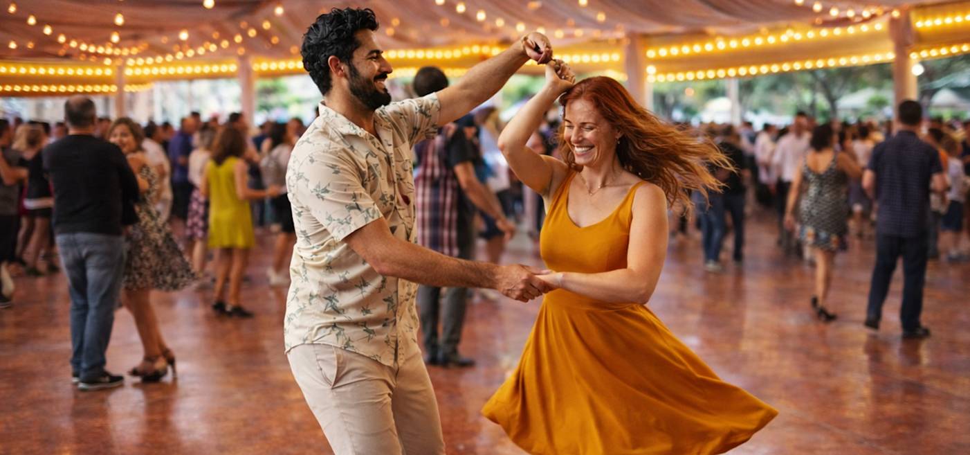 En man och en kvinna dansar tillsammans under ljusslingor på ett utomhusevenemang, omgivna av andra människor på ett täckt dansgolv.
