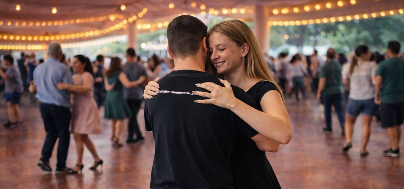 Ett par dansar tätt under ljusslingor i en fullsatt, täckt utomhuslokal med andra par dansande i bakgrunden.