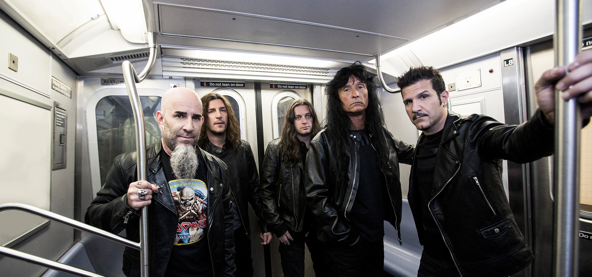Fem män i svarta skinnjackor står i ett tunnelbanetåg, håller i ledstängerna och tittar in i kameran.
