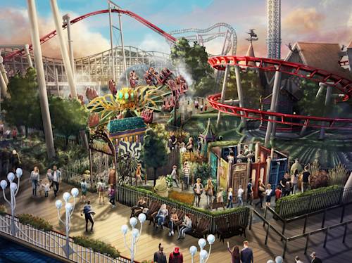 People walk and gather in an amusement park with roller coasters and rides, surrounded by greenery and various attractions under a partly cloudy sky.