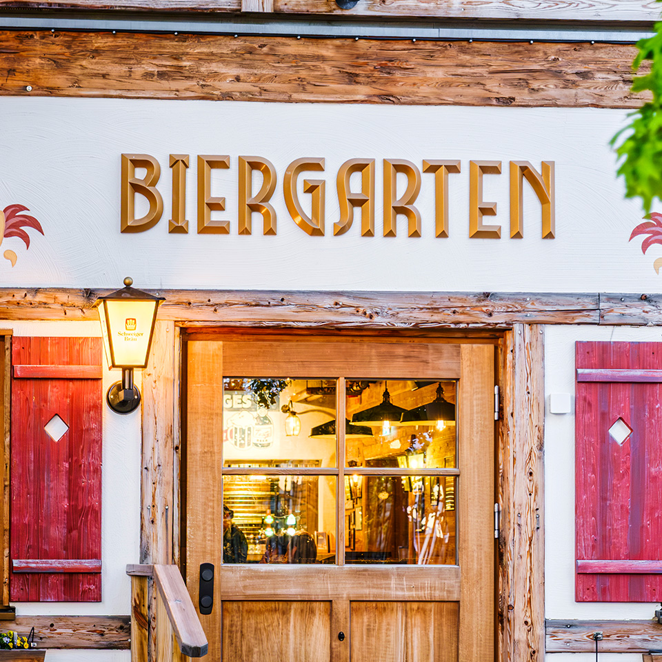 Wooden door and windows beneath a sign reading "Biergarten" on the exterior of a traditional German-style building.