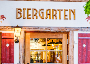 Wooden door and windows beneath a sign reading "Biergarten" on the exterior of a traditional German-style building.