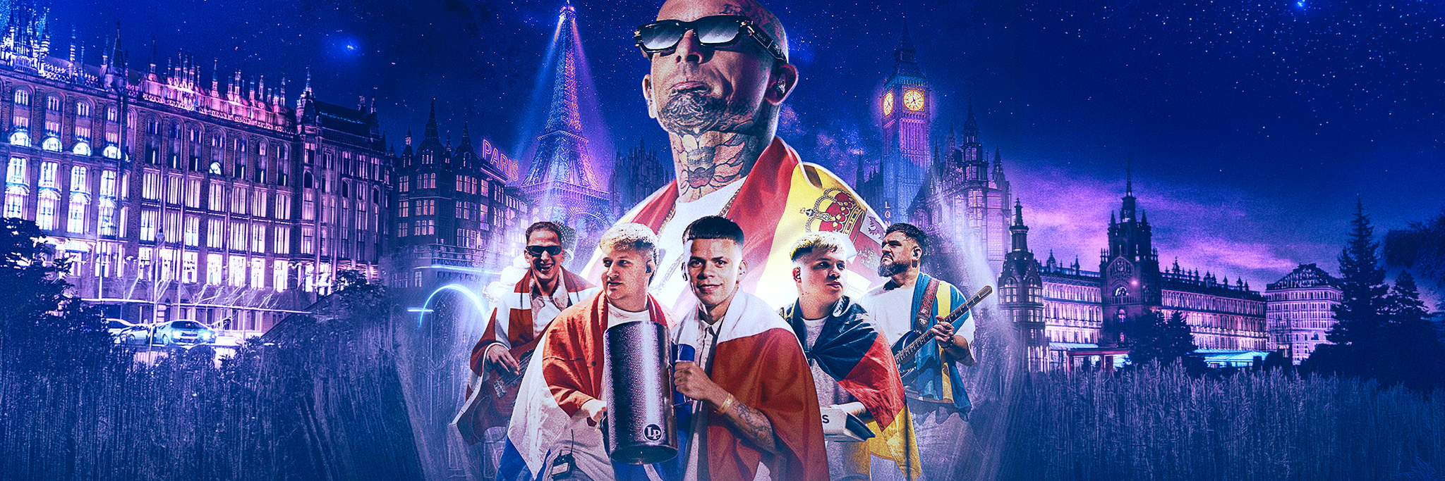 A group of men, some holding musical instruments and draped in flags, stand in front of city landmarks at night with a blue and purple sky in the background.