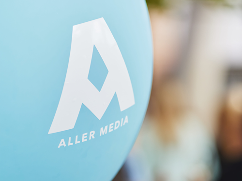 A close-up of a blue balloon with a white “A” and the text “ALLER MEDIA” printed on it.