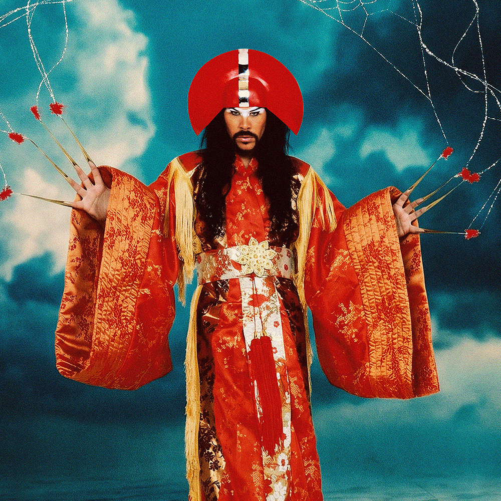 En person iklädd en utsmyckad röd mantel och huvudbonad poserar med utsträckta armar mot en dramatisk molnig bakgrund, med pilar hängande i luften nära händerna.