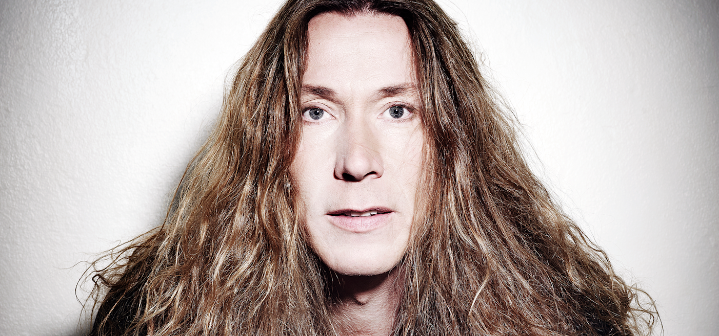 Person with long, wavy hair standing against a plain white background, facing forward with a neutral expression.