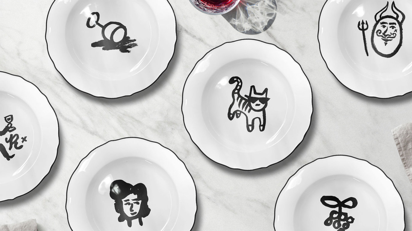 A series of white dining plates on a marble surface, each plate with its own unique Frenchy illustration printed in the centre.