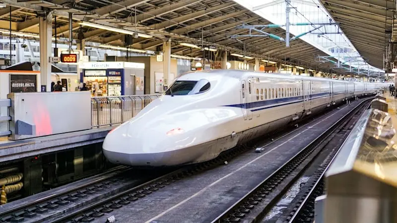 White Shinkansen with blue streaks on its carriages arriving at a Tokyo station.