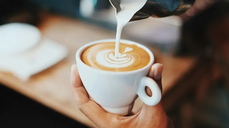 A barista pouring milk into a latte to make coffee art