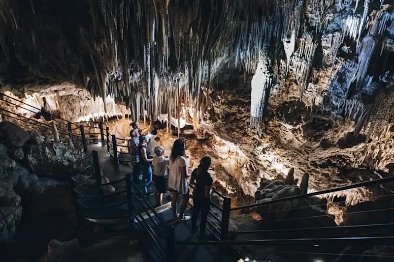Visitors exploring illuminated limestone formations on a staircase inside Ngilgi Cave, Margaret River, Western Australia.