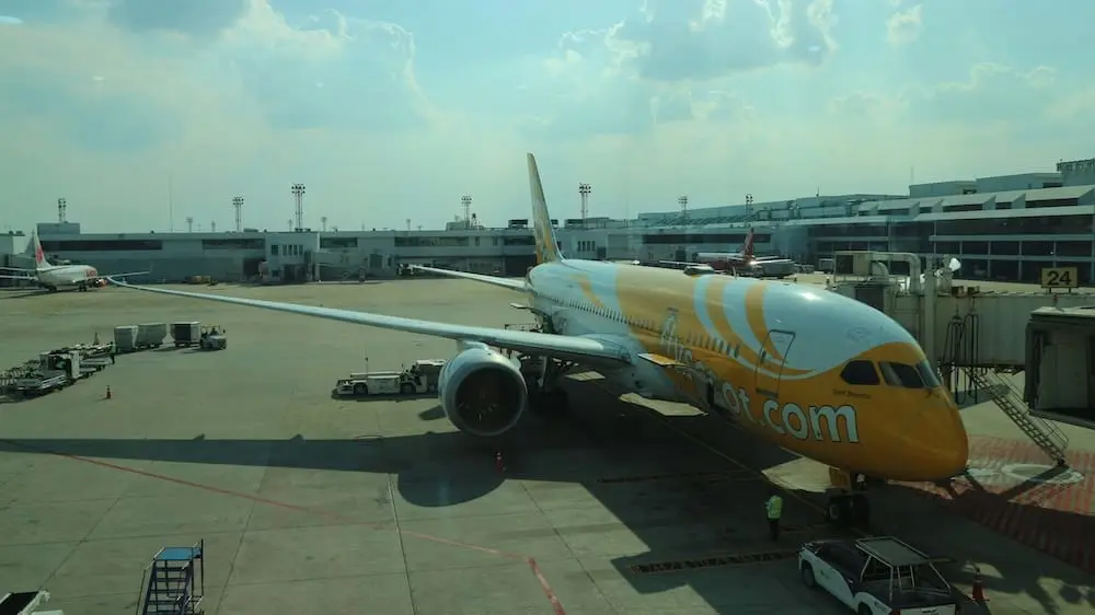Scoot Boeing 787 Dreamliner parked at Don Mueang International Airport gate under cloudy sky, preparing for boarding.