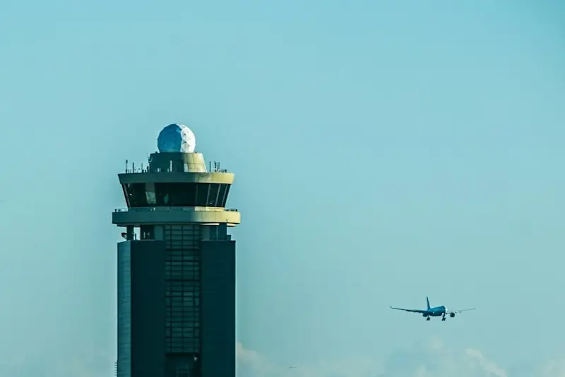 Air traffic control tower at Narita International Airport with a radar dome on top, as a commercial airplane approaches for landing.